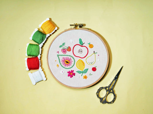 Fruity Fiesta Embroidery Kit with apple, pear, lemon, and floral designs, shown with colorful threads and embroidery scissors on a yellow background.