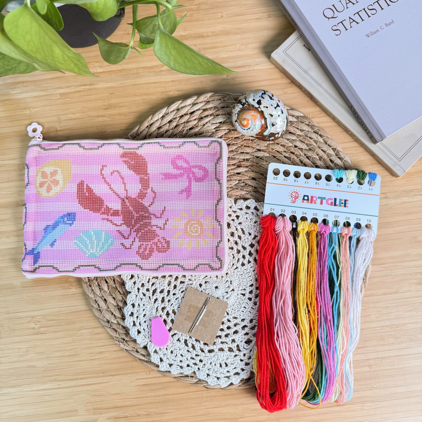 Lucky Catch Coast Half-Stitch Kit flat lay, featuring a finished lobster pouch alongside colorful embroidery threads, needle, and accessories, styled on a wooden surface with coastal decor.
