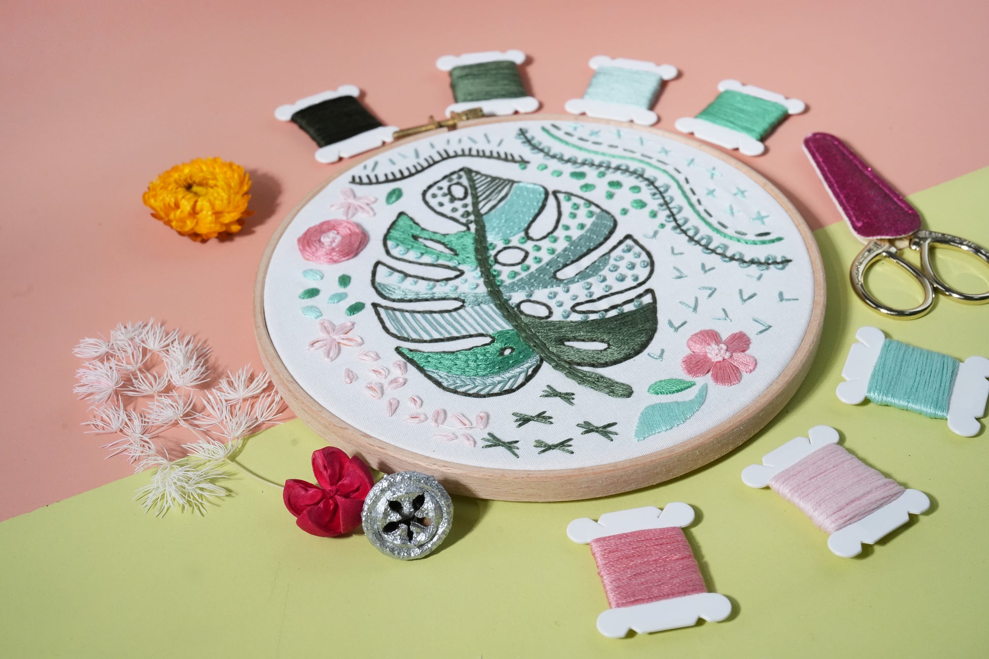 Close-up of monstera embroidery hoop showing detailed green stitches with threads and scissors.
