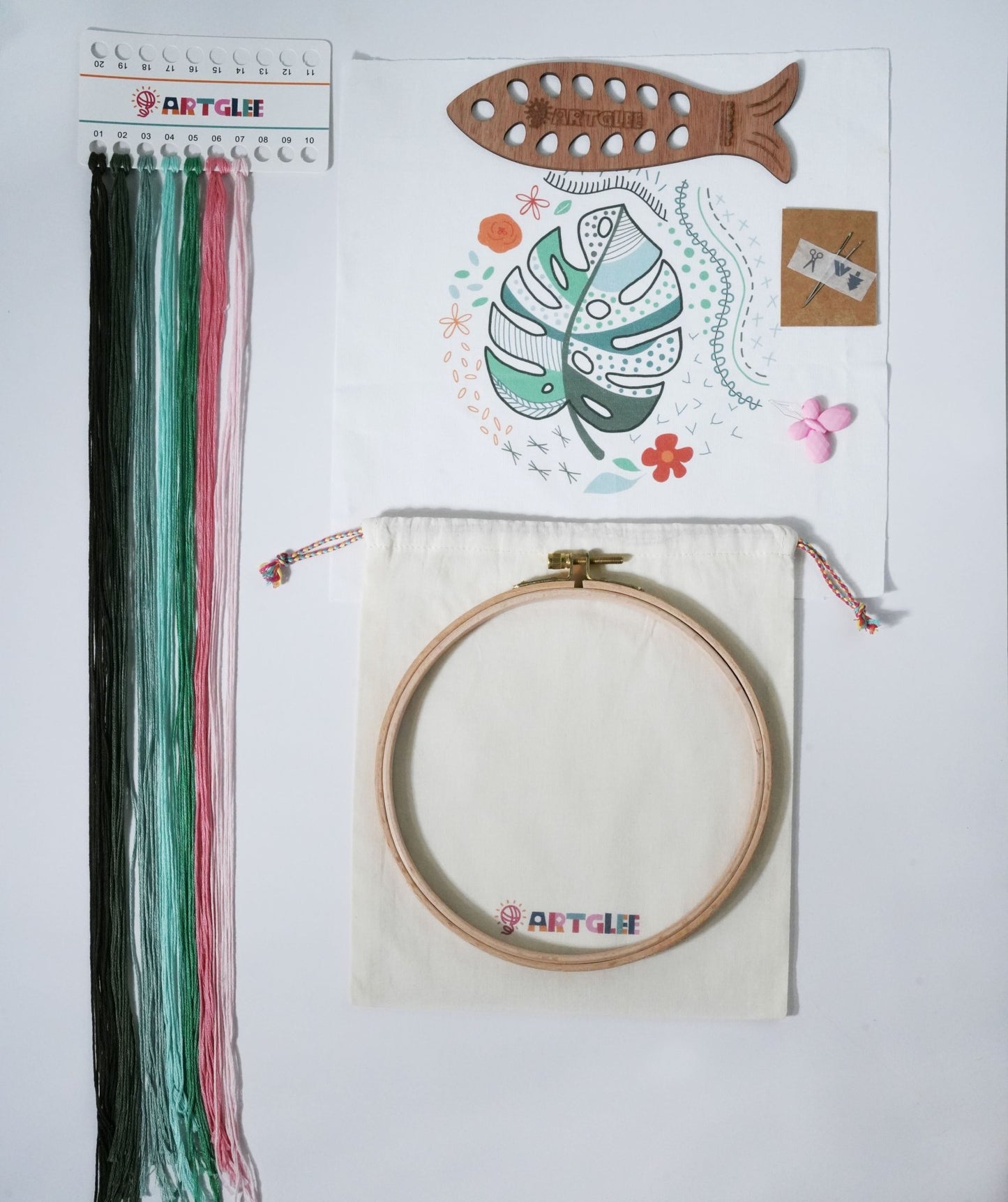 Full monstera embroidery beginner kit contents with printed fabric, colorful threads, fish-shaped thread board, hoop, and cotton bag.