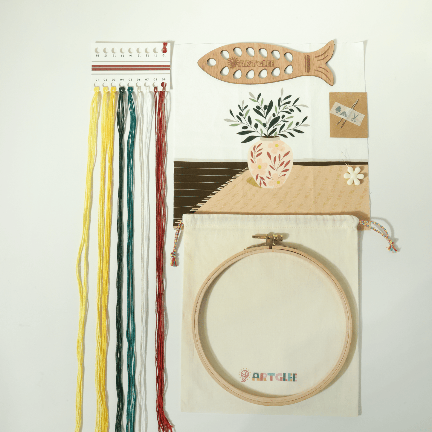 Full olive leaf vase embroidery kit contents with printed fabric, threads, fish-shaped thread board, hoop, and cotton bag.
