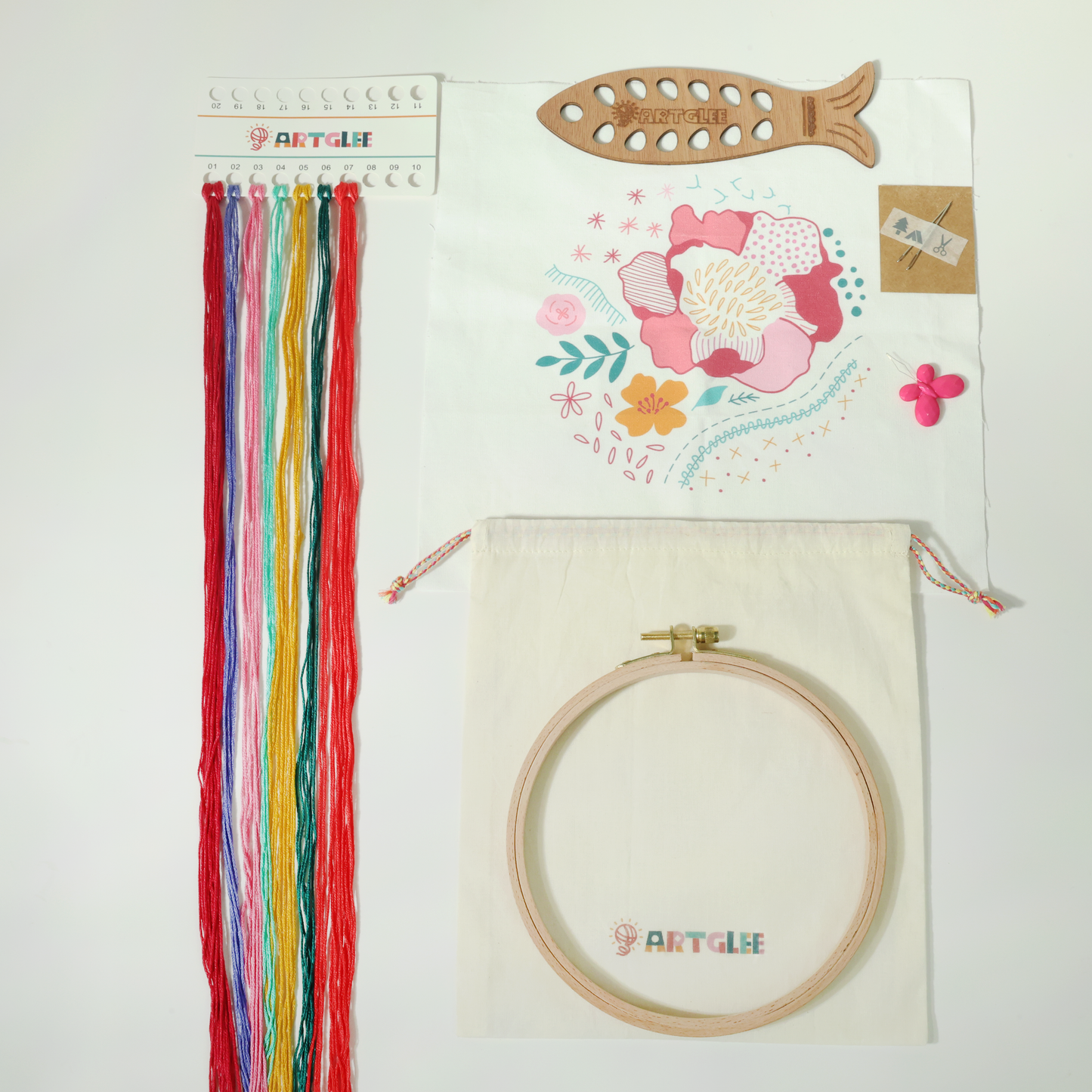 Full embroidery kit contents with printed fabric, colorful threads, hoop, fish-shaped thread board, and cotton bag.