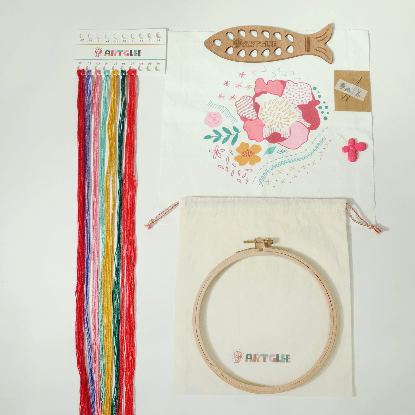 Full embroidery kit contents with printed fabric, colorful threads, hoop, fish-shaped thread board, and cotton bag.