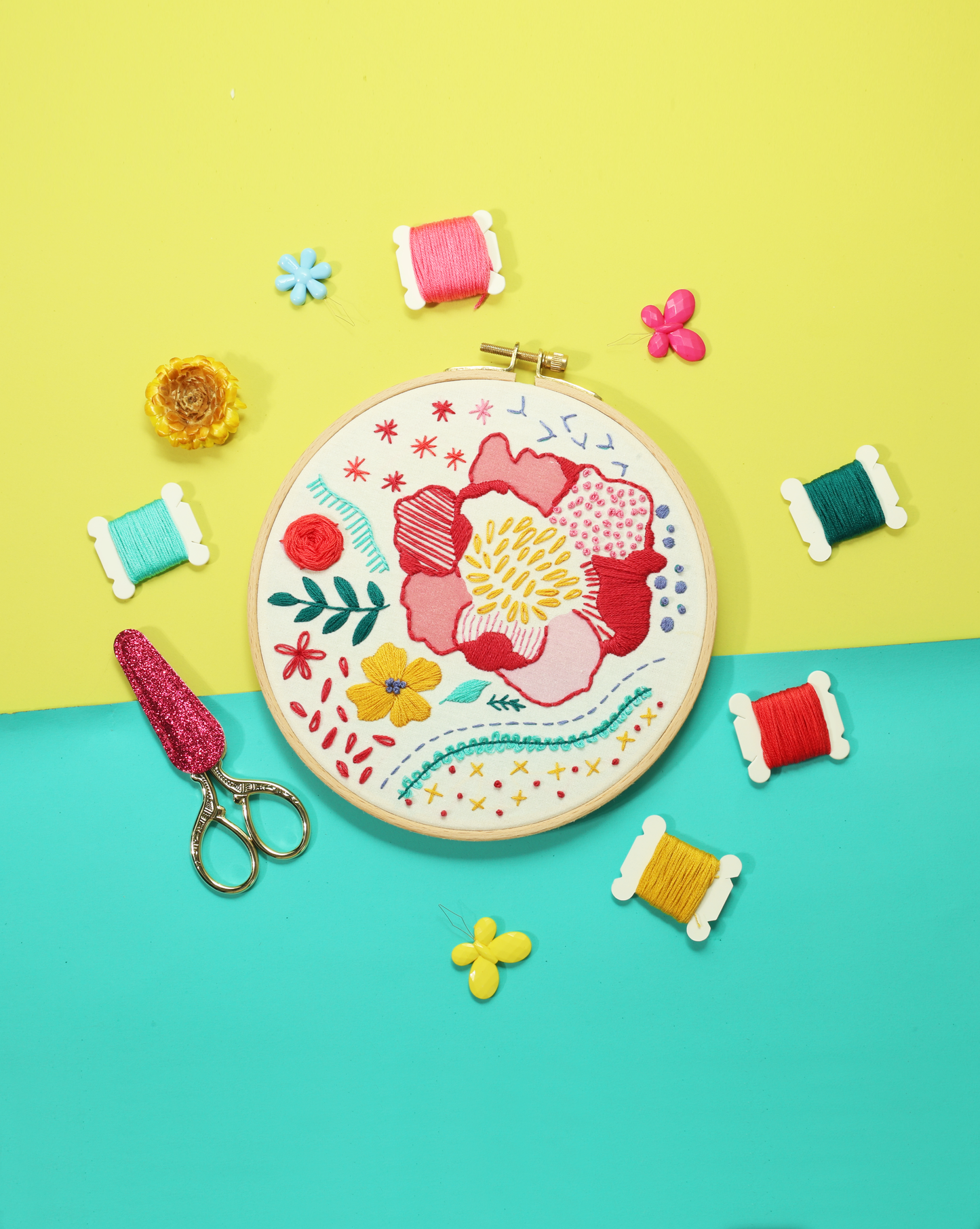 Beginner embroidery kit flat lay with floral hoop, threads, and scissors on vibrant yellow and teal background.
