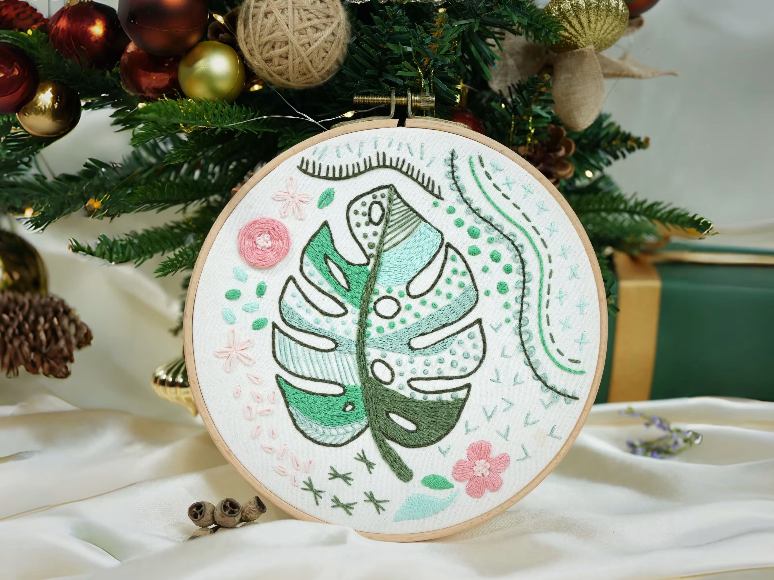 Close-up of Artglee's Monstera Leaf Embroidery Kit, featuring a beautifully stitched leaf design, surrounded by festive Christmas decorations. This kit offers a relaxing and creative way to add handmade charm to your holiday season.
