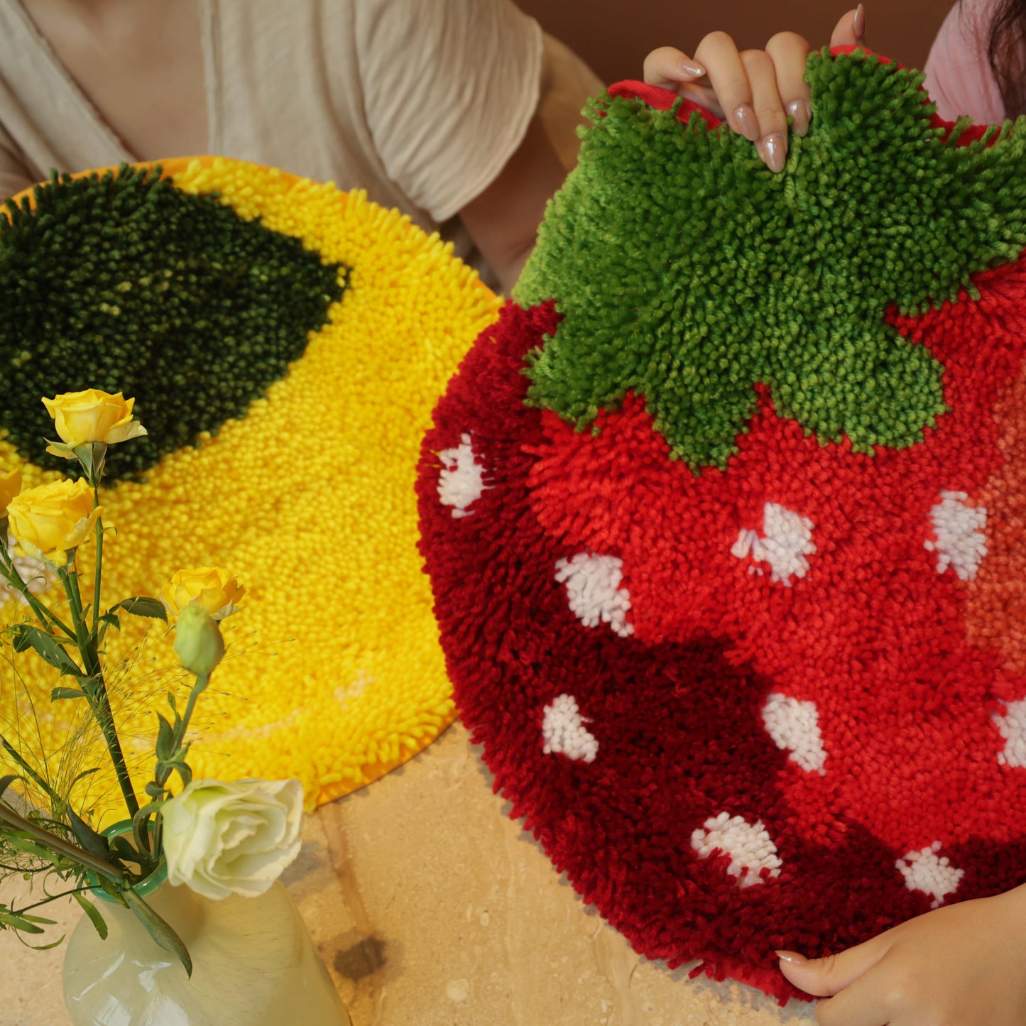 Two people holding up finished Sunny Lemon and Sweet Strawberry latch hook rugs side by side, showing their bright colors.