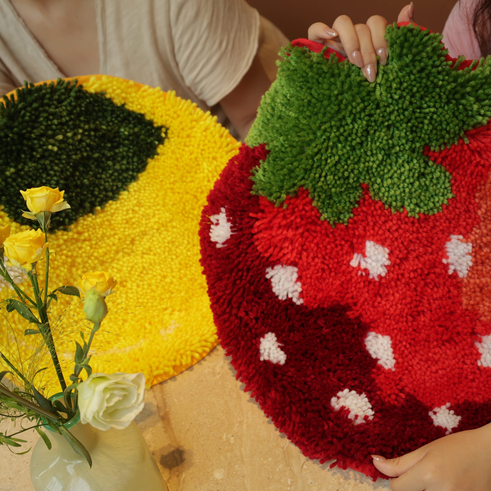 Two people holding up finished Sunny Lemon and Sweet Strawberry latch hook rugs side by side, showing their bright colors.