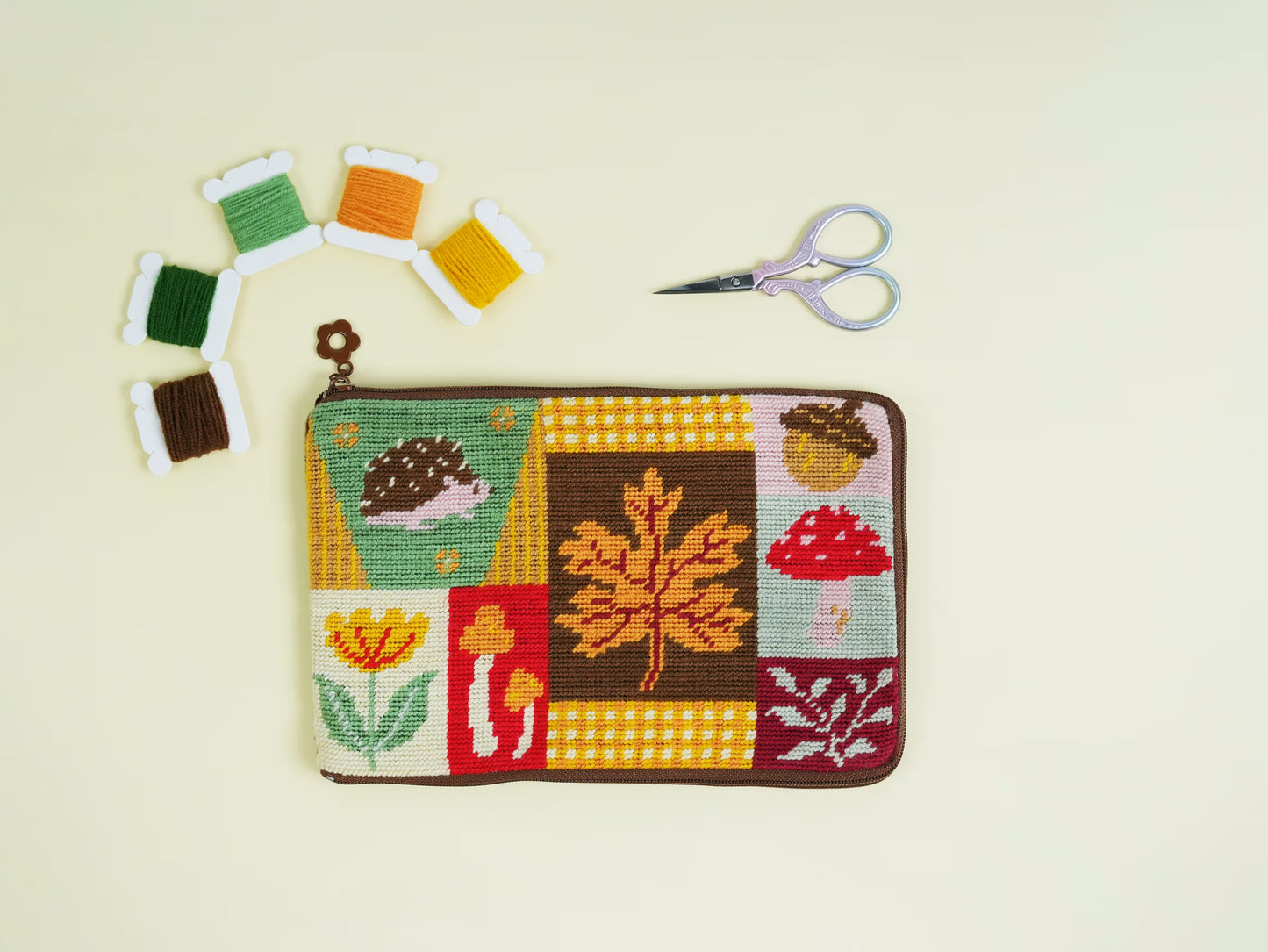 Autumn Forest Half-Stitch Bag Kit flat lay, featuring a patchwork-style embroidered pouch with autumn leaves, mushrooms, flowers, and woodland motifs on a light background.
