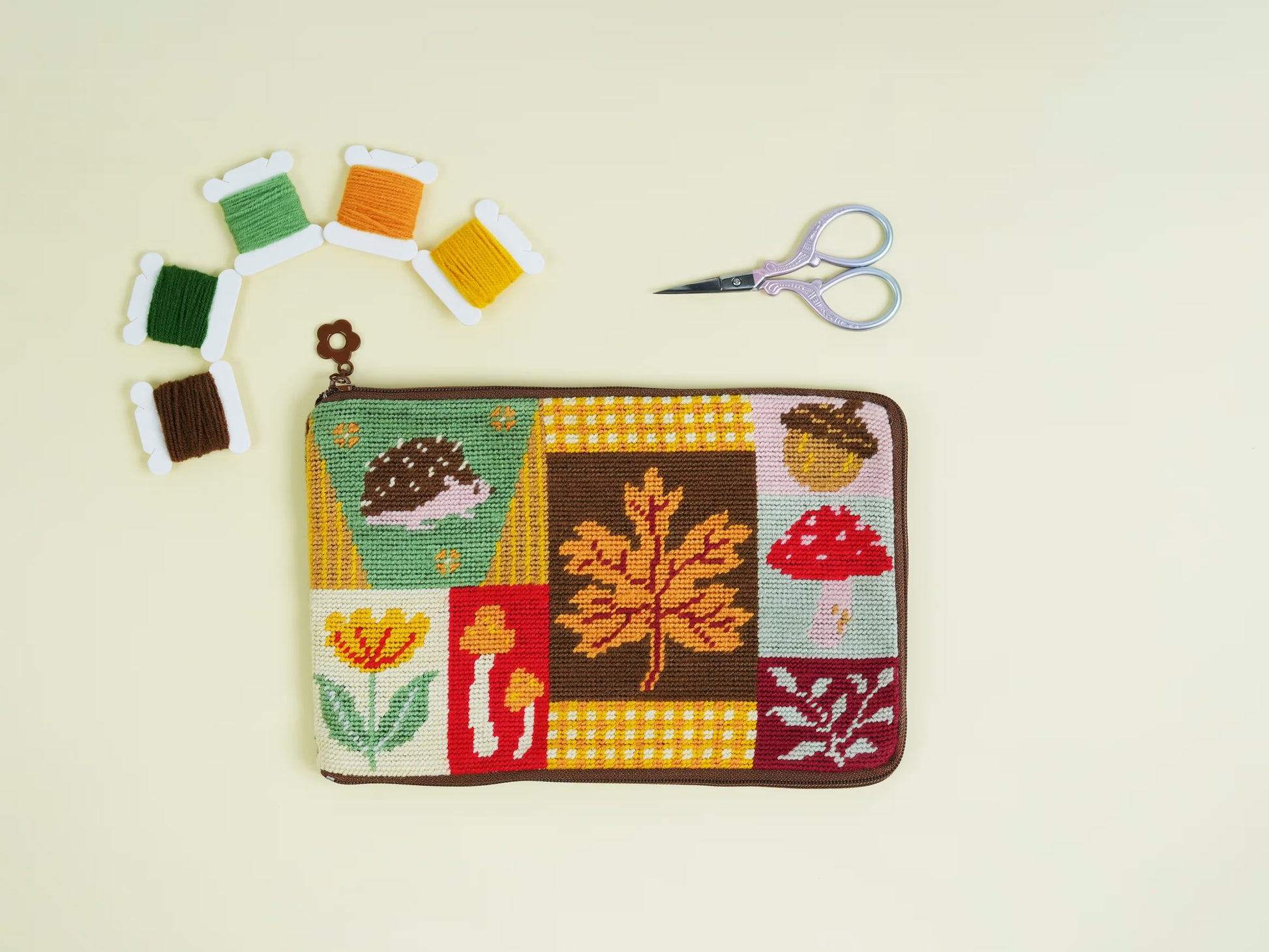 Autumn Forest Half-Stitch Bag Kit flat lay, featuring a patchwork-style embroidered pouch with autumn leaves, mushrooms, flowers, and woodland motifs on a light background.
