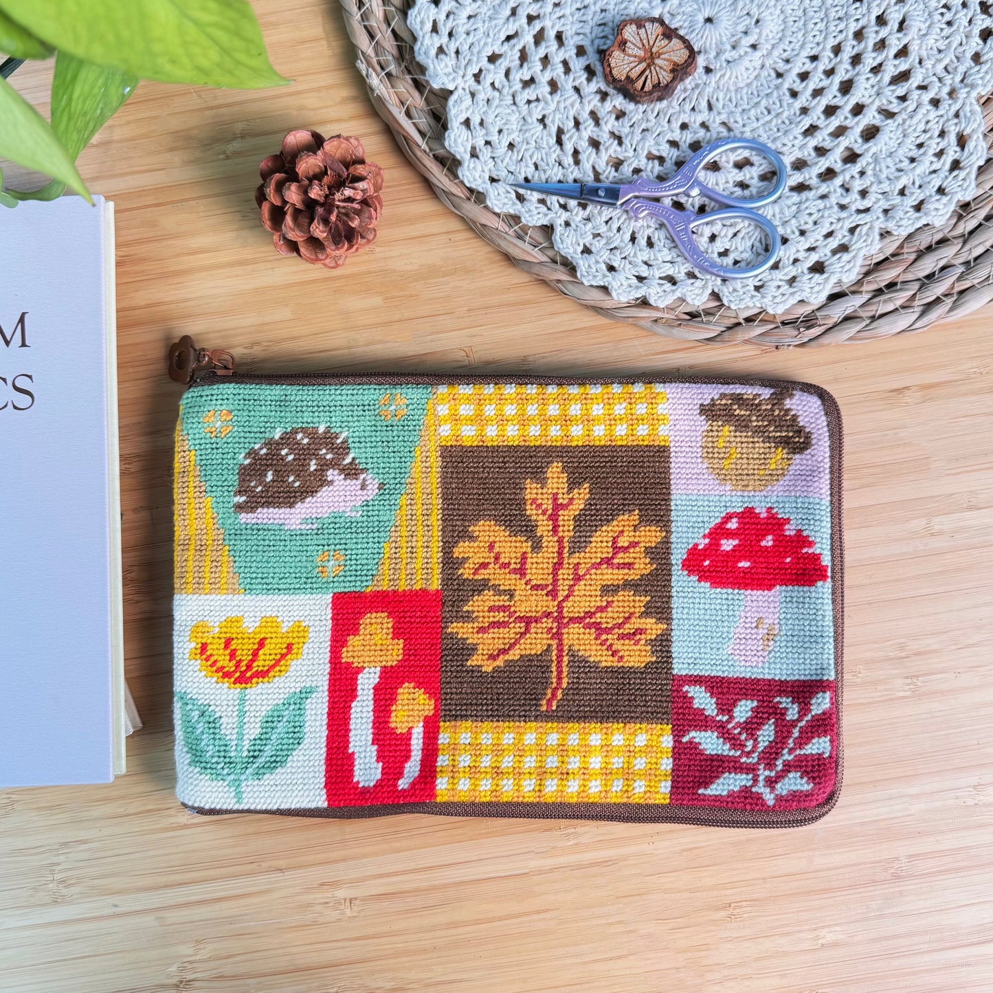 Autumn Forest Half-Stitch Bag Kit pouch laid flat on a wooden surface, featuring a patchwork design with autumn leaves, mushrooms, florals, embroidery textures, and sewing tools.
