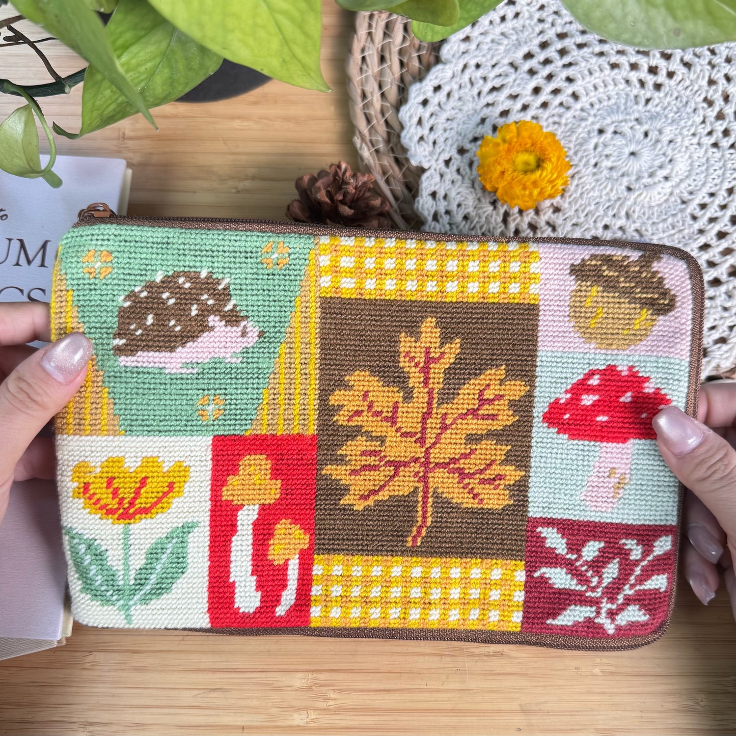 Autumn Forest Half-Stitch Bag Kit pouch held in hands, featuring a patchwork design with autumn leaves, mushrooms, florals, embroidery textures, and a cozy handmade look.
