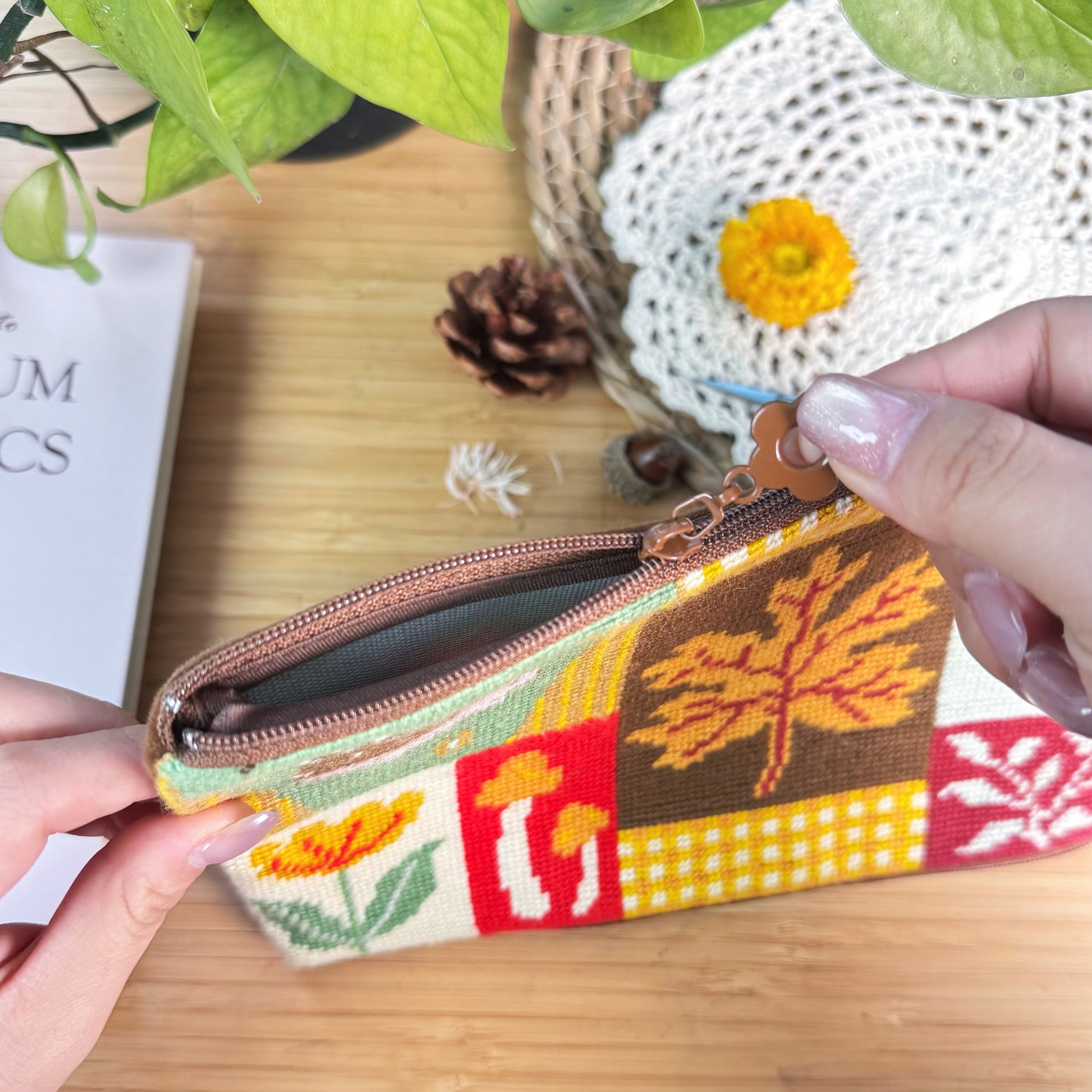 Autumn Forest Half-Stitch Bag Kit zipper detail, showing the pouch opened by hand with visible lining, sturdy zipper, and autumn patchwork embroidery design.
