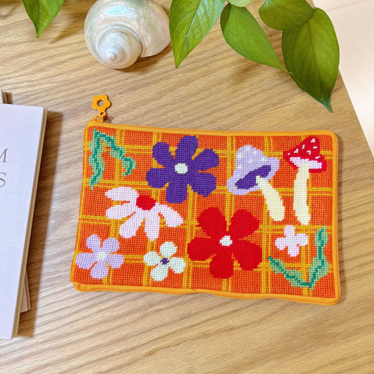 Handmade Bloom Daisy Half-Stitch Pouch with floral and mushroom patterns on orange grid background