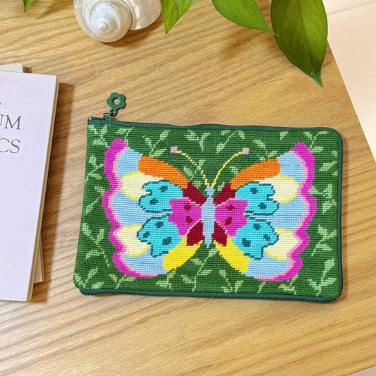 Finished Butterfly Garden Half-Stitch Kit pouch laying flat on a wooden table with a green leafy background pattern.