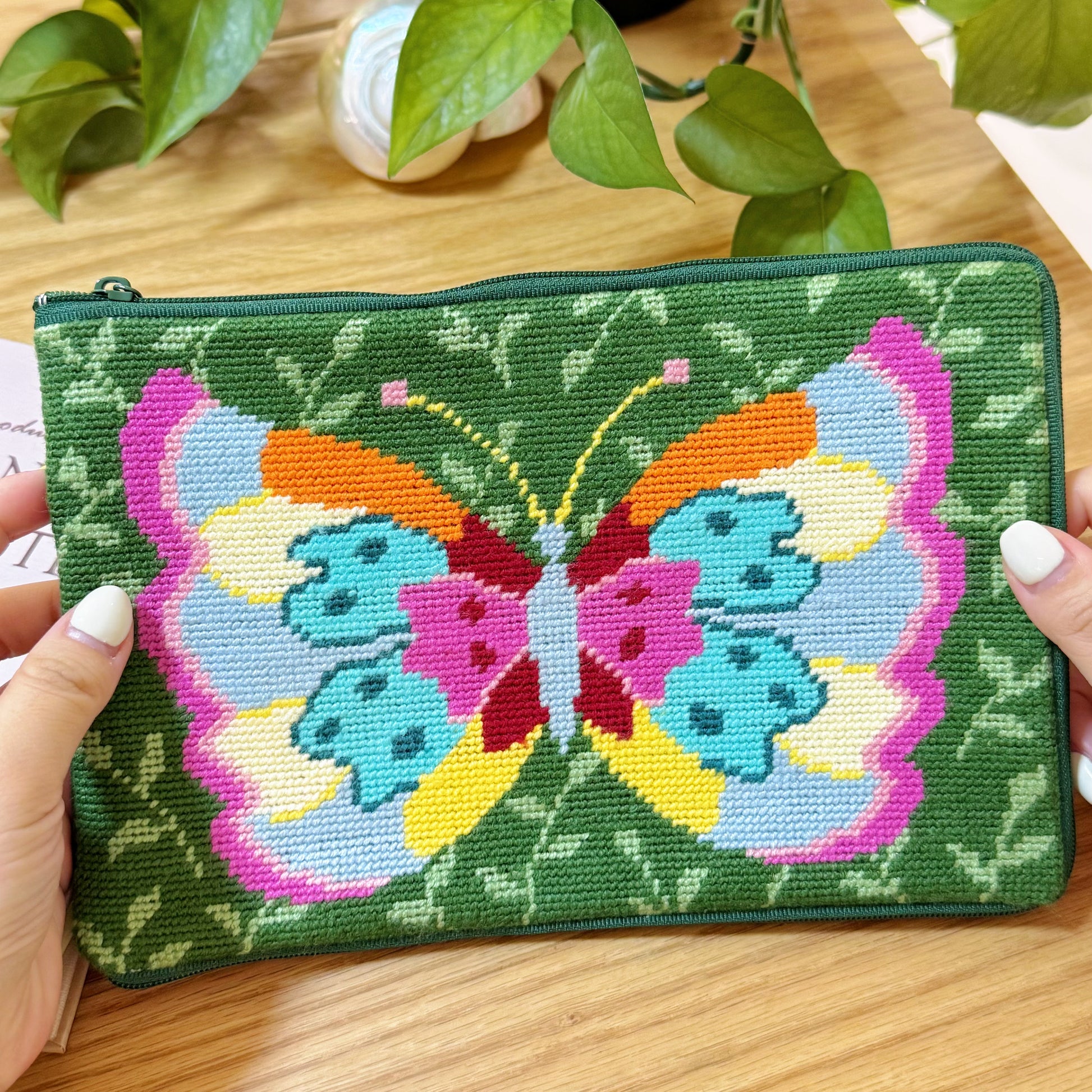 Close-up of the finished Butterfly Garden Half-Stitch Kit pouch being held in two hands, showing the colorful butterfly design.