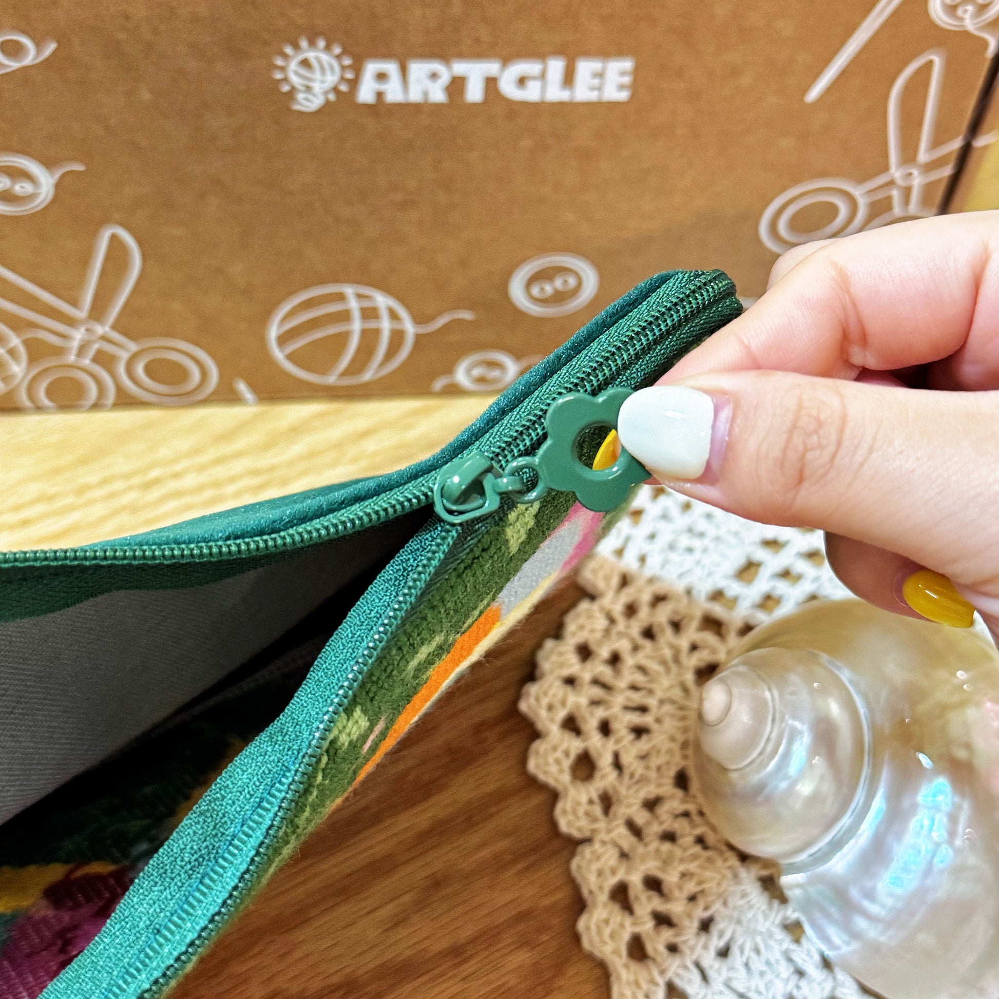 Hand holding and opening the zipper of the Butterfly Garden Half-Stitch Kit pouch, showing interior detail.