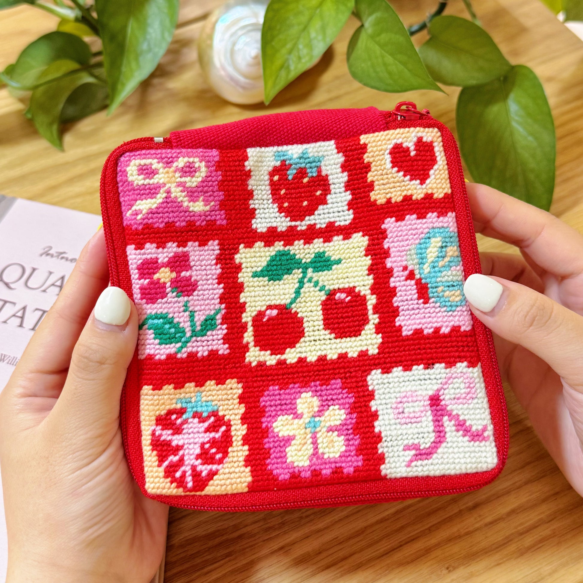 Close-up of Cherry Love Half-Stitch Kit pouch held in hands, showing colorful patchwork strawberry and cherry designs.