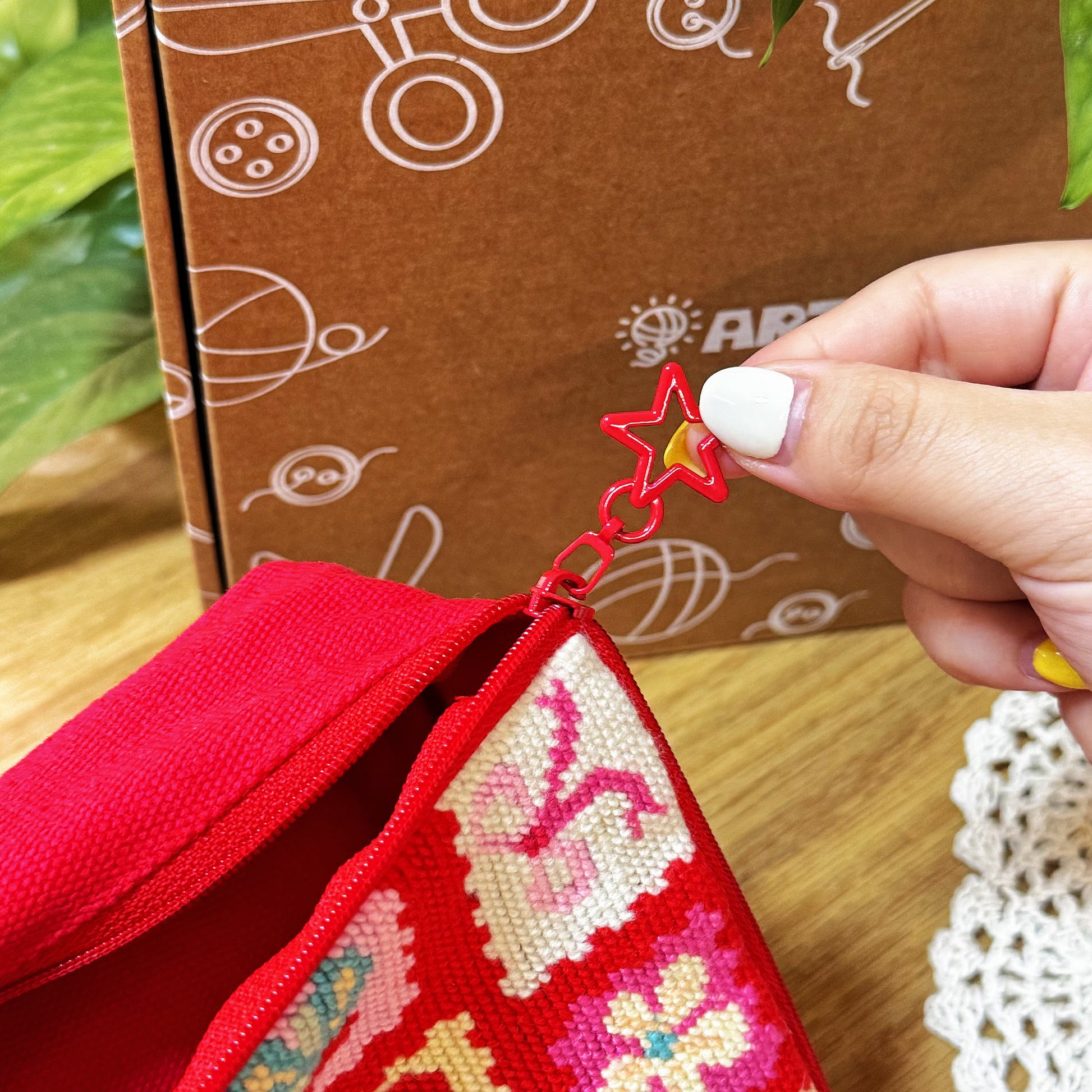 Hand holding the red star-shaped zipper pull of Cherry Love Half-Stitch Kit pouch.