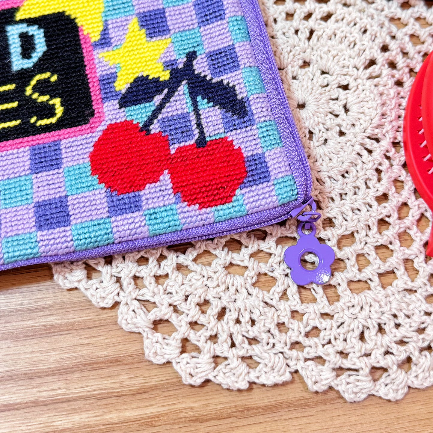 Close-up of cherry embroidery and purple flower-shaped zipper pull on the Good Times Half-Stitch Kit pouch.