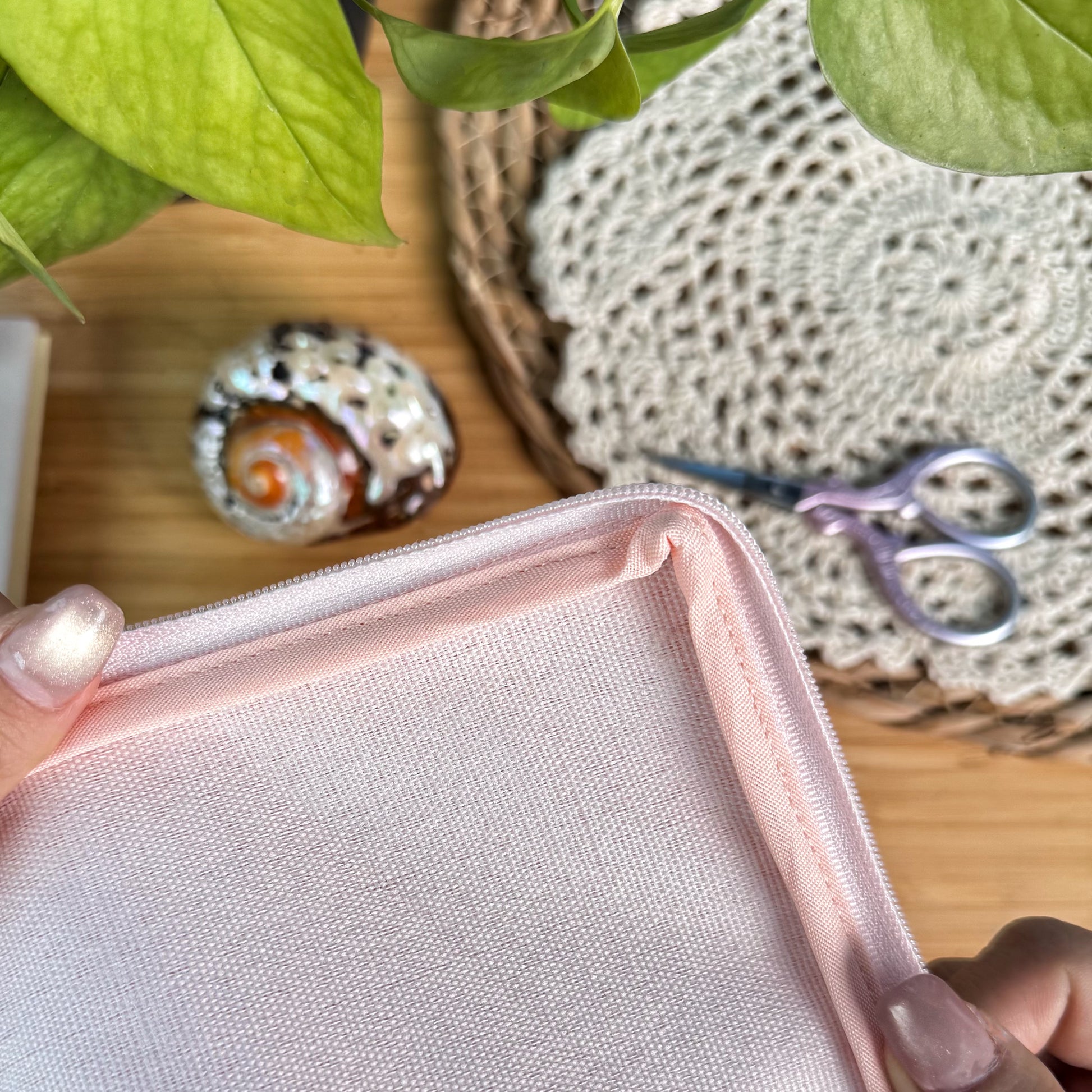 Lucky Catch Coast Half-Stitch Kit pouch lining detail, showing the soft pink fabric interior held in hands, styled on a wooden surface with coastal decor.
