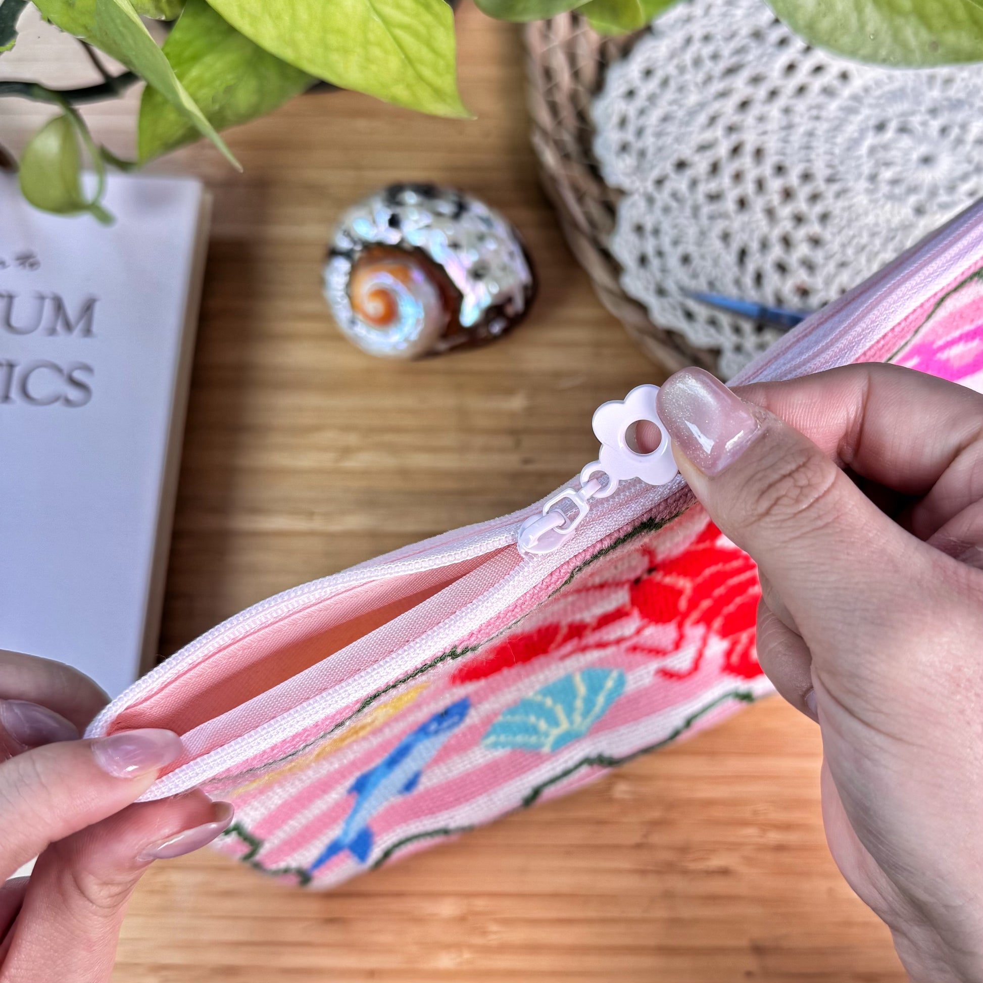 Lucky Catch Coast Half-Stitch Kit zipper detail, showing the pouch being opened by hand with a smooth zipper and soft pink lining, styled on a wooden surface with coastal decor.
