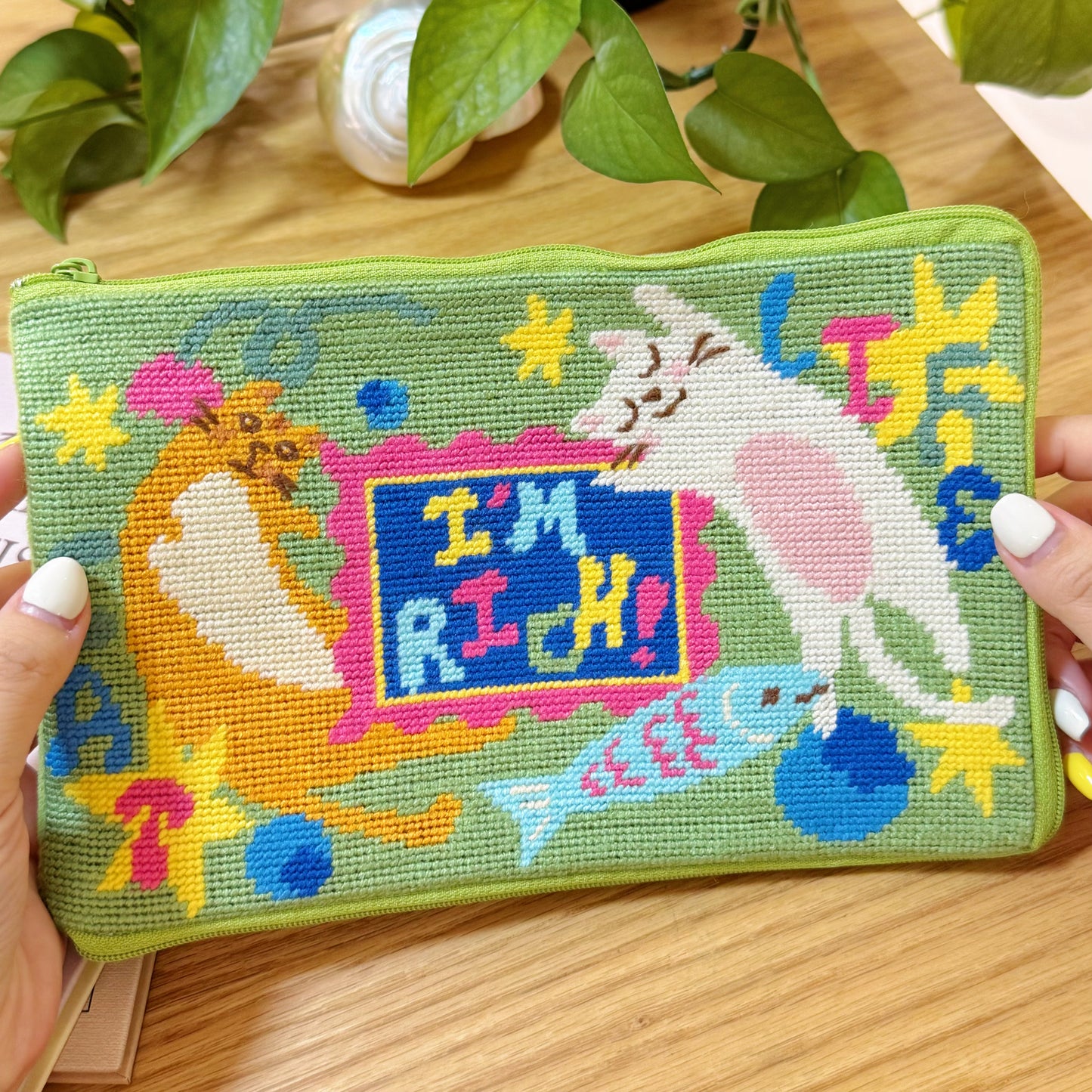 Hand holding the Lucky Cats half-stitch zipper pouch, showing detailed embroidery of cats and fish.