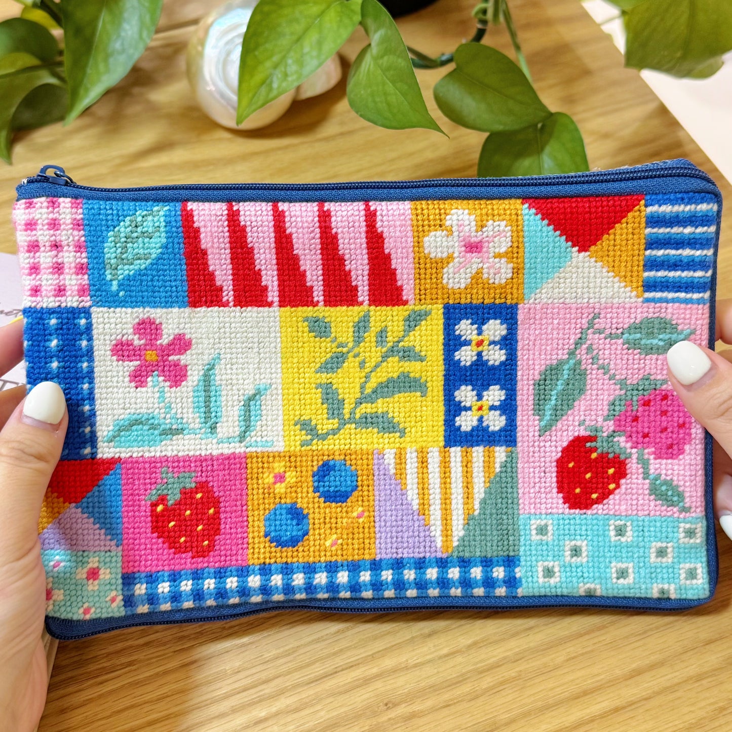 Patchwork Garden Half-Stitch Kit pouch held in hands, showing vibrant strawberry and floral needlework