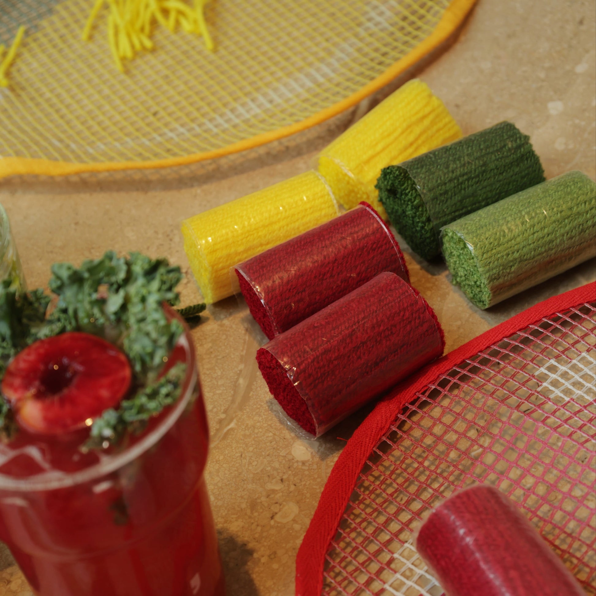 Close-up of red, green, and yellow yarn rolls next to the strawberry latch hook kit mesh canvas, ready for use.