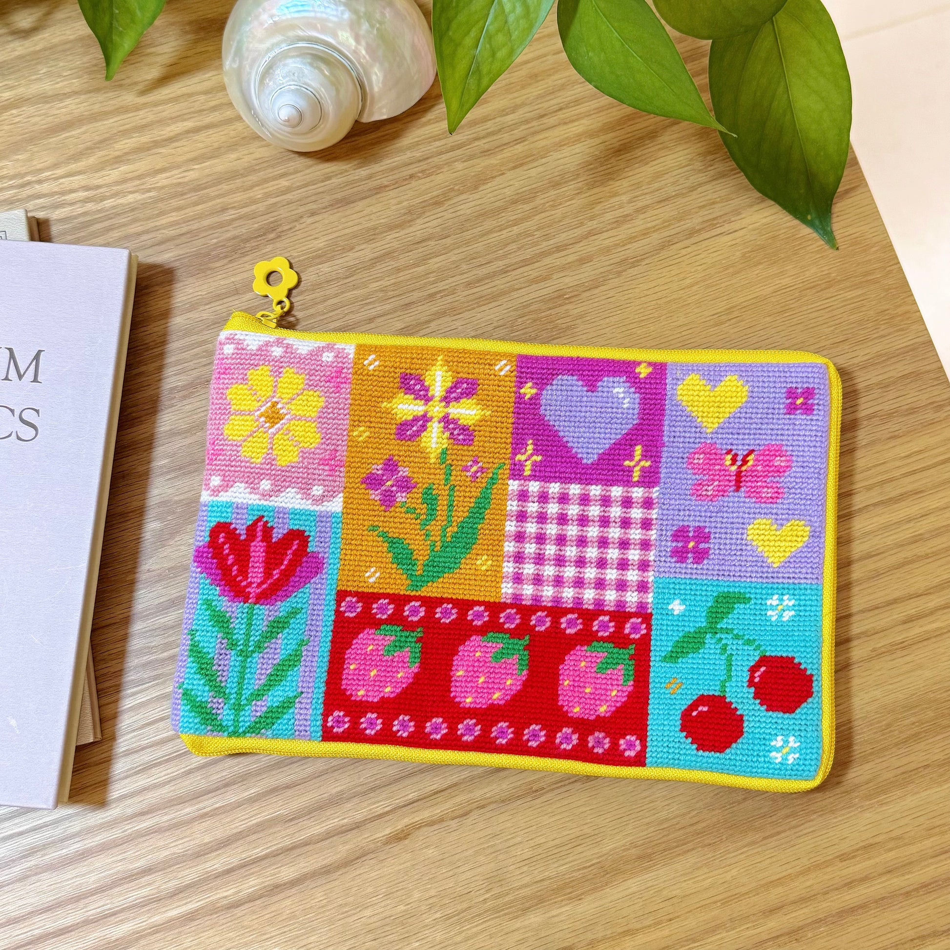 Colorful patchwork half-stitch pouch with flowers, hearts, strawberries, and cherries on a wooden table.