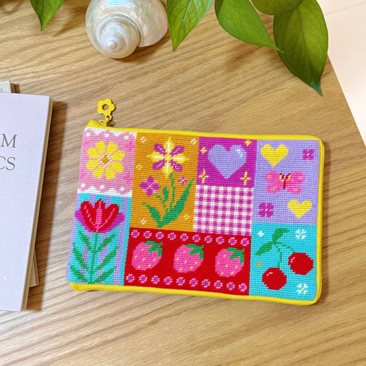 Colorful patchwork half-stitch pouch with flowers, hearts, strawberries, and cherries on a wooden table.
