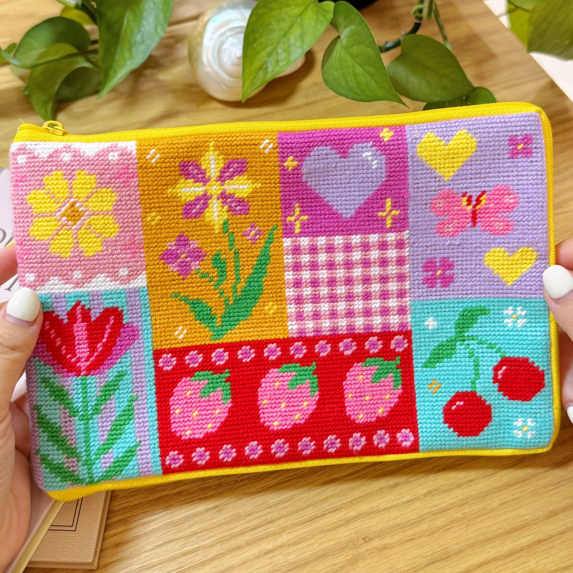 Handmade half-stitch pouch held in hands, featuring vibrant floral and fruit patchwork design.
