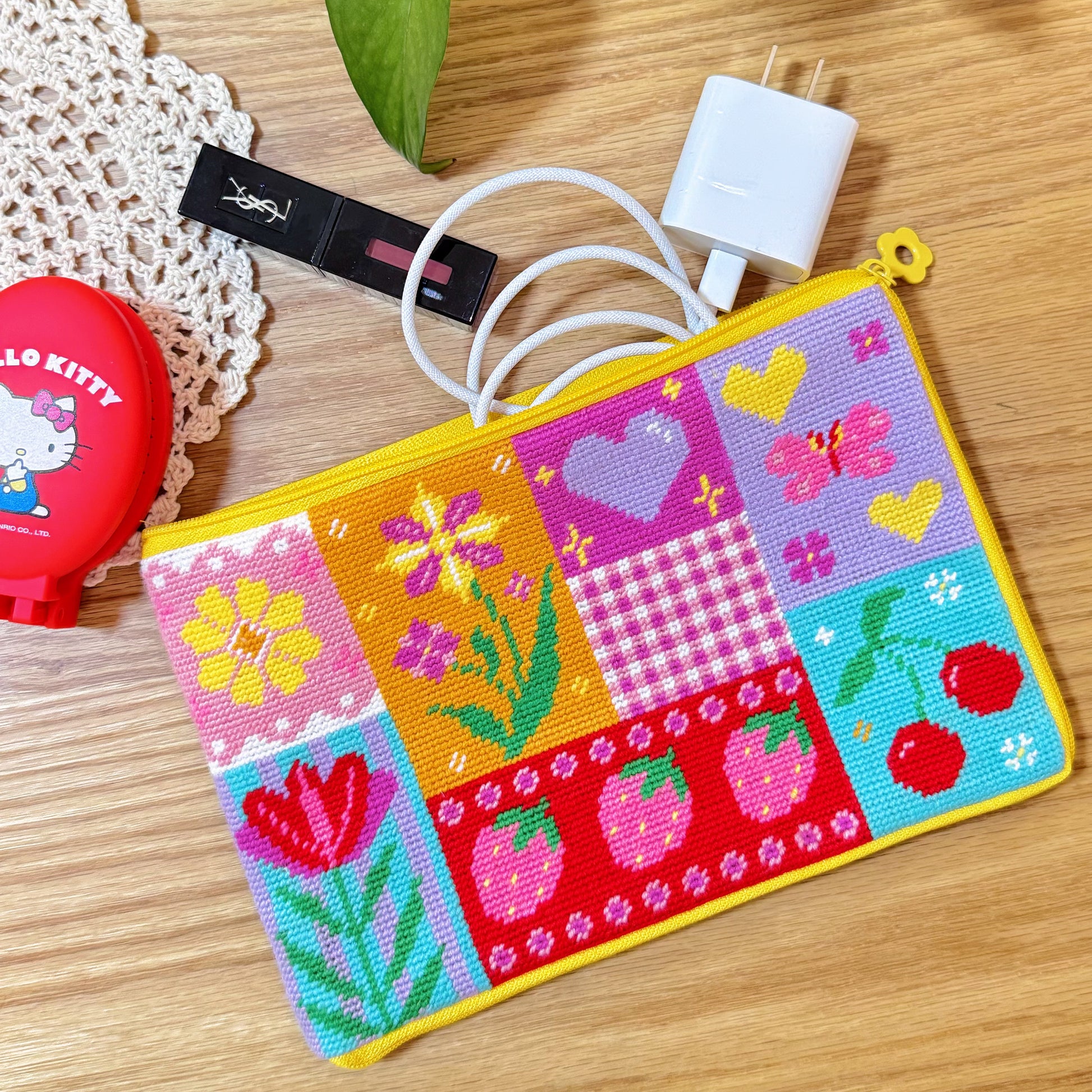 Sunny Bloom pouch used for storage, holding charger and cosmetics on a wooden table.