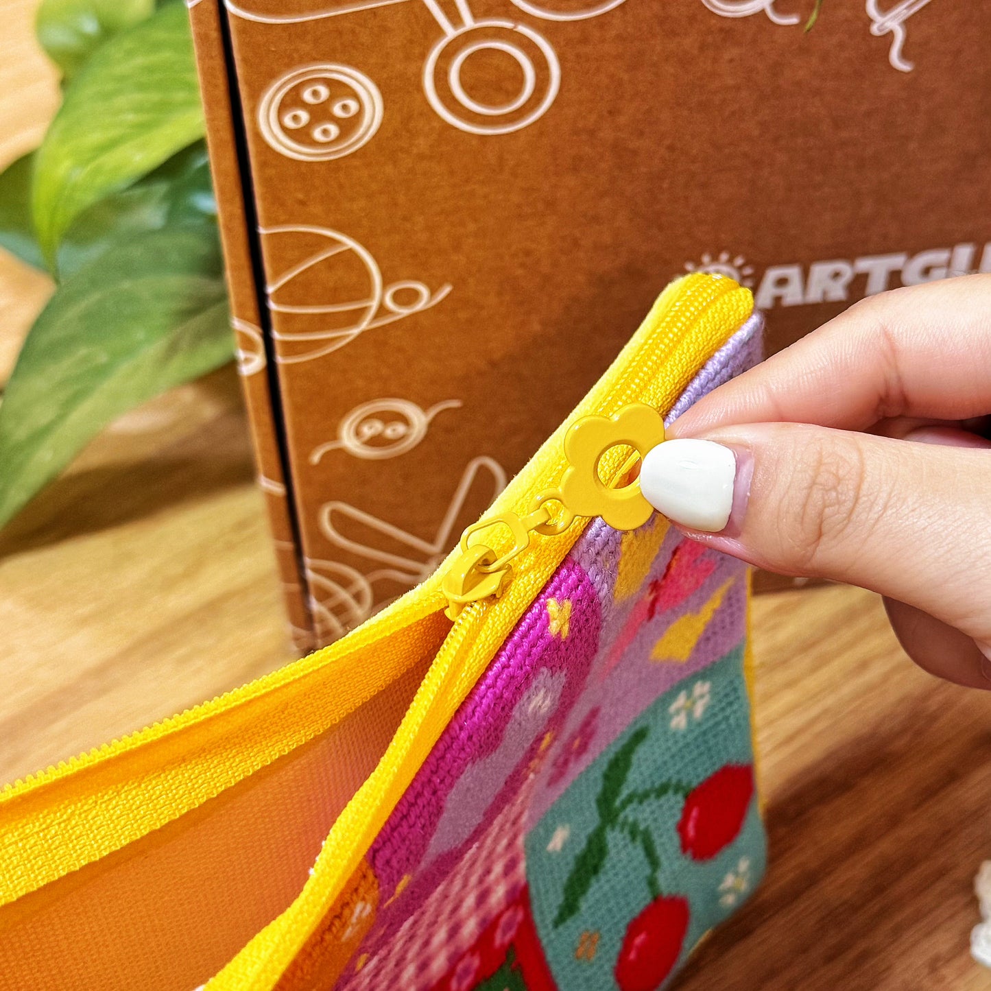 Hand opening yellow zipper of Sunny Bloom patchwork pouch, showing stitching detail.