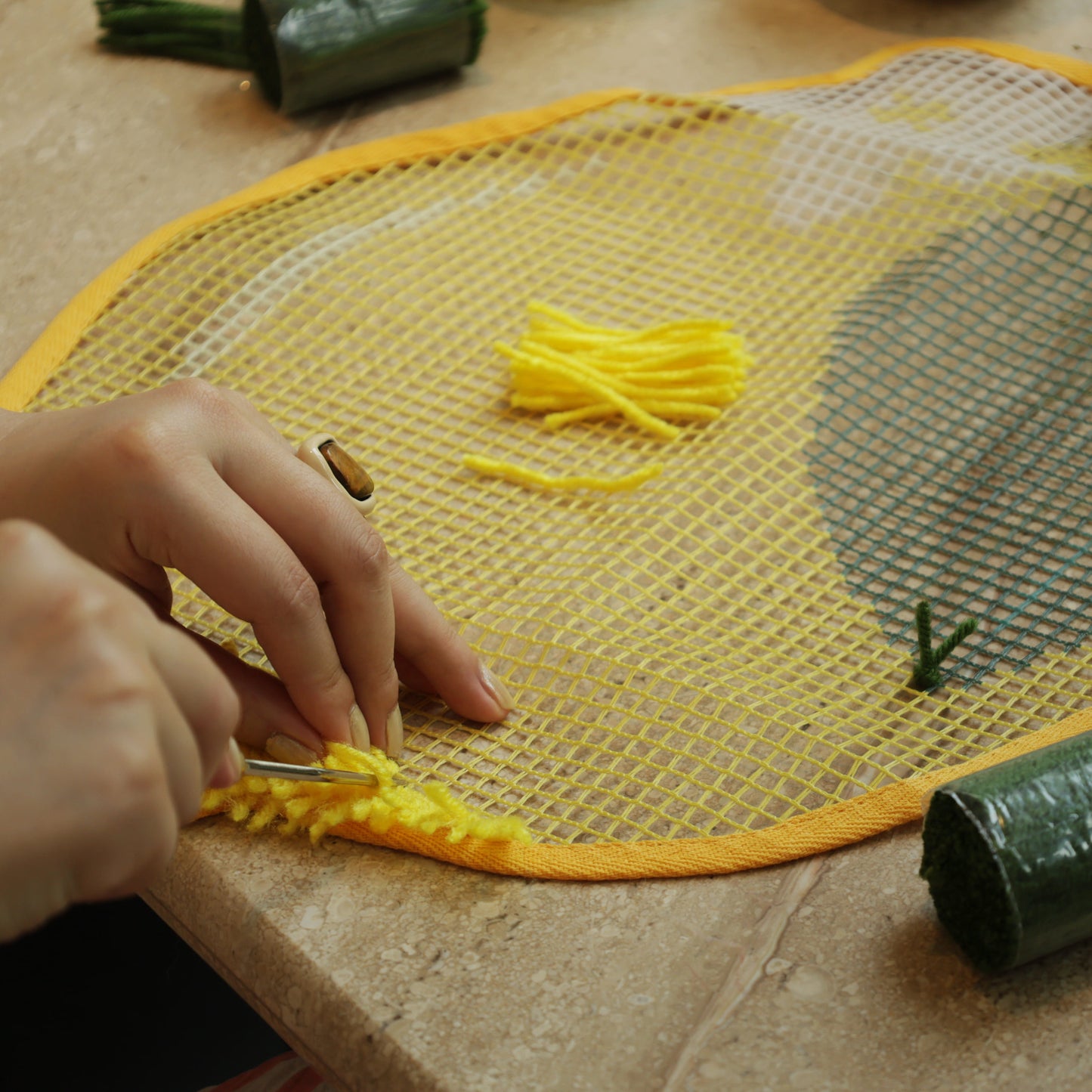Close-up of a crafter hooking yellow yarn into the Sunny Lemon latch hook canvas with a metal latch hook tool.