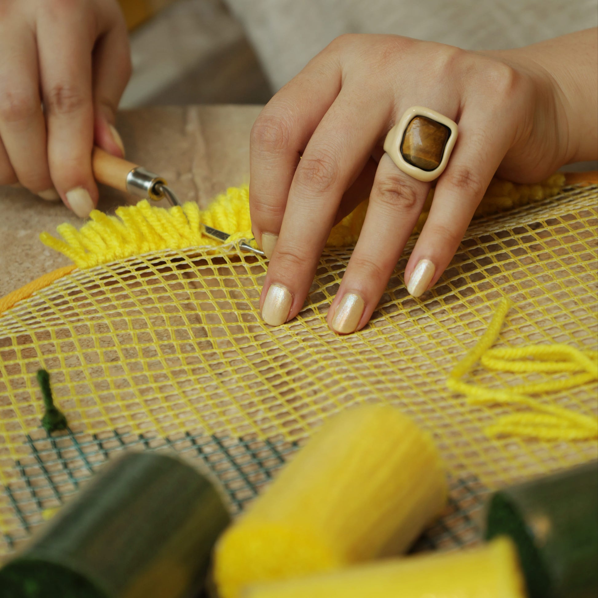 Detailed view of hands securing yellow yarn into the Sunny Lemon latch hook kit canvas, showing precision work.