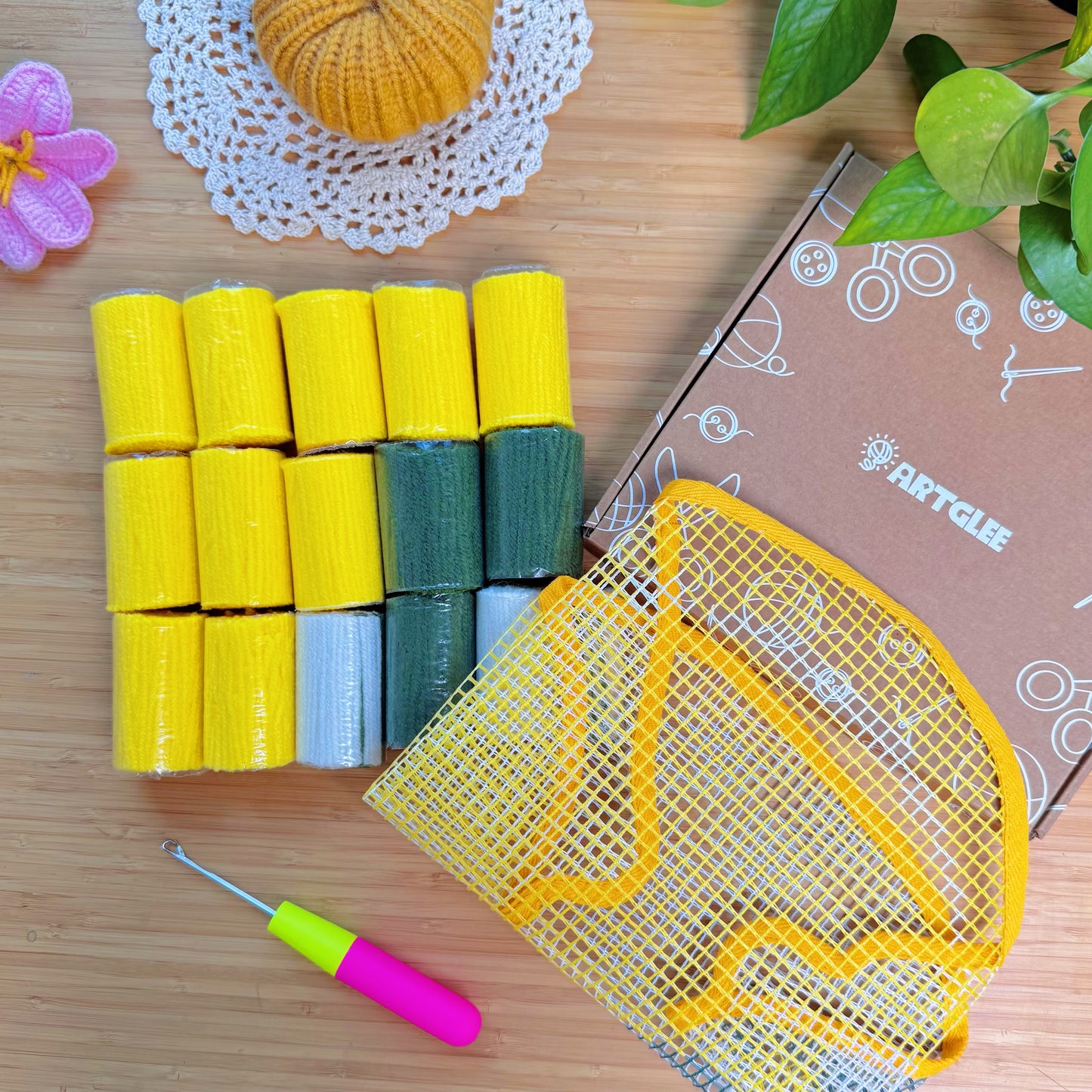 Unpacked Sunny Lemon latch hook kit showing yellow, green, and white yarn rolls, latch hook tool, and mesh canvas with printed lemon design.