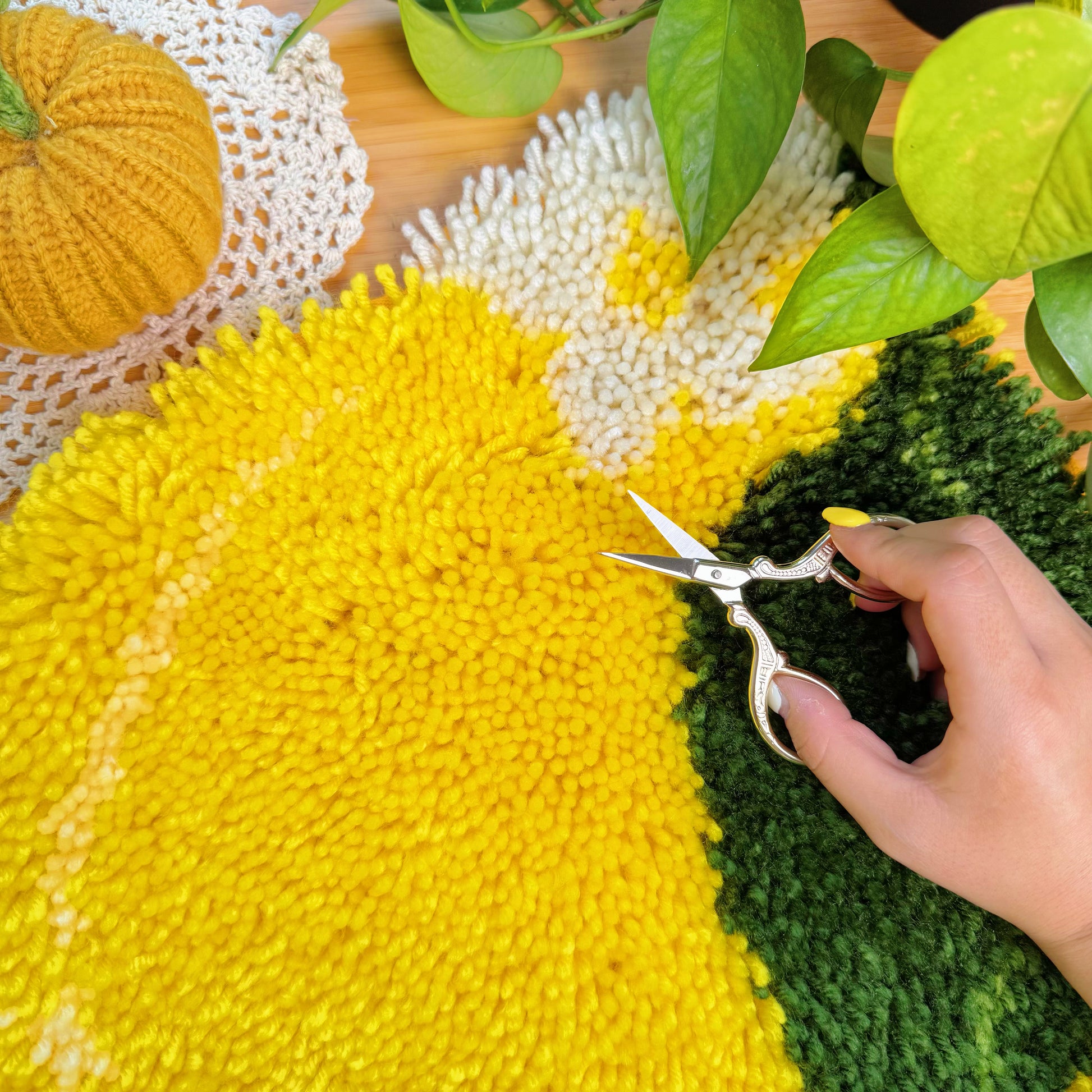 Close-up of a hand using scissors to trim yarn on the Sunny Lemon latch hook rug to refine the shape and texture.
