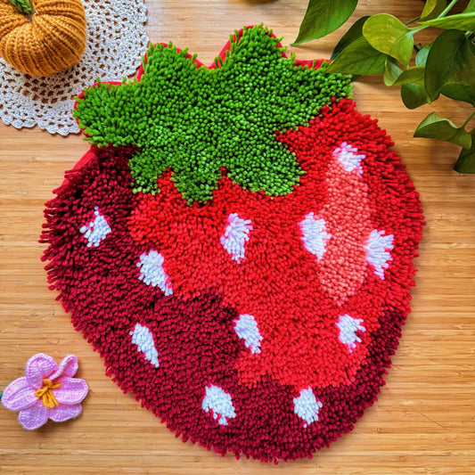 Finished Sweet Strawberry latch hook mat with vibrant red and green yarn on wooden table