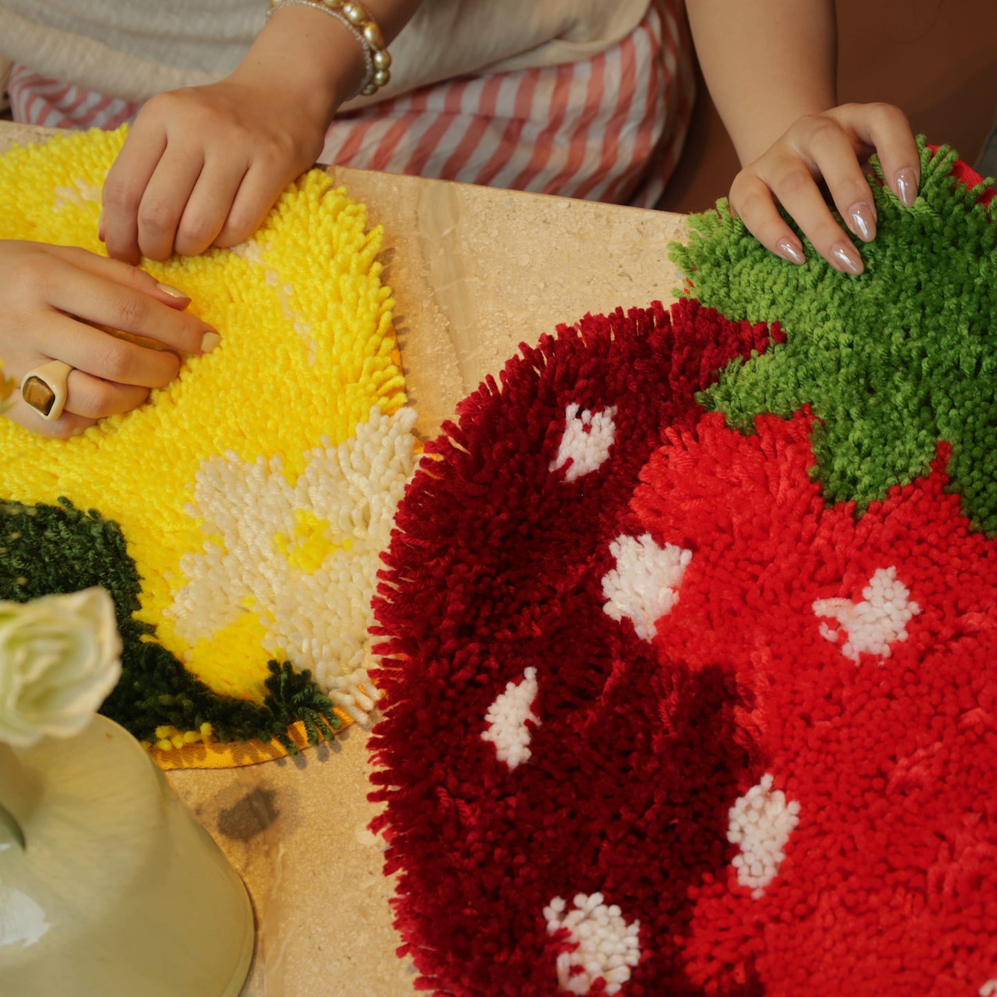 Two hands showing progress on the Sweet Strawberry and Sunny Lemon latch hook kits side by side on a tabletop.