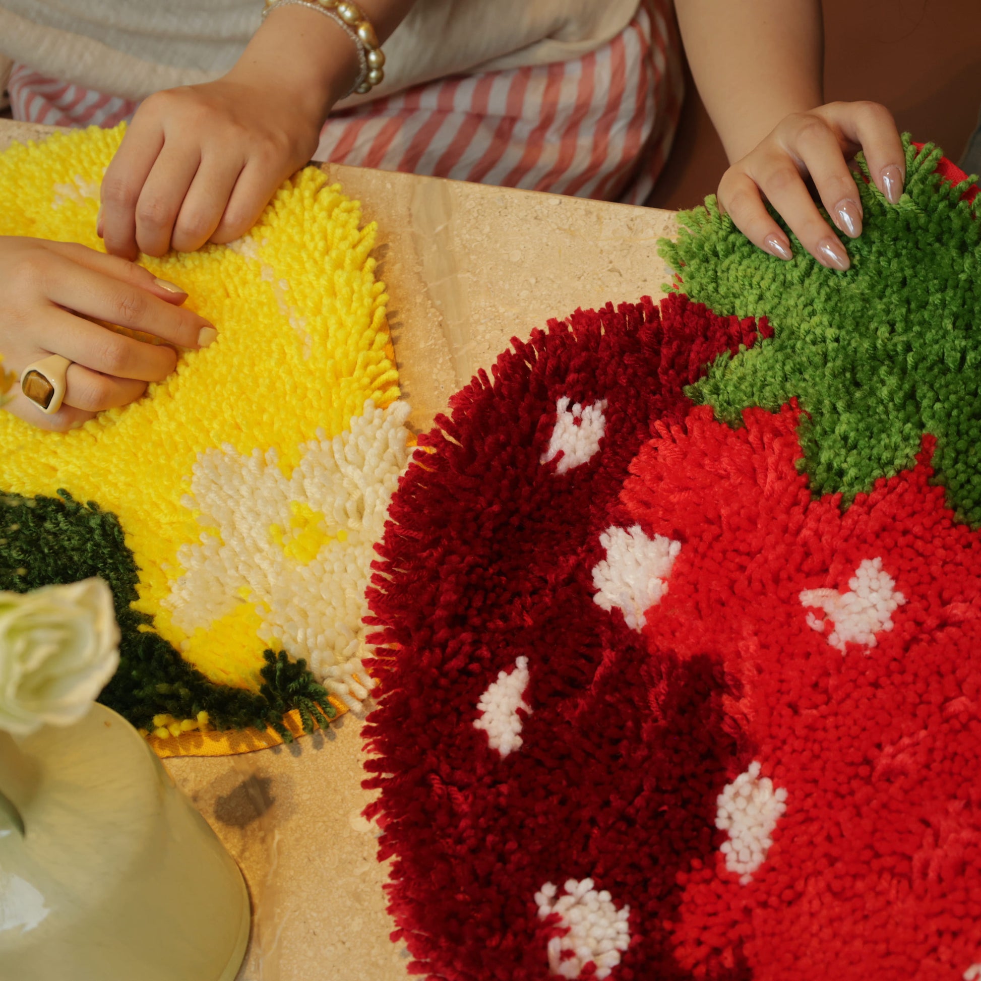 Two hands showing progress on the Sweet Strawberry and Sunny Lemon latch hook kits side by side on a tabletop.